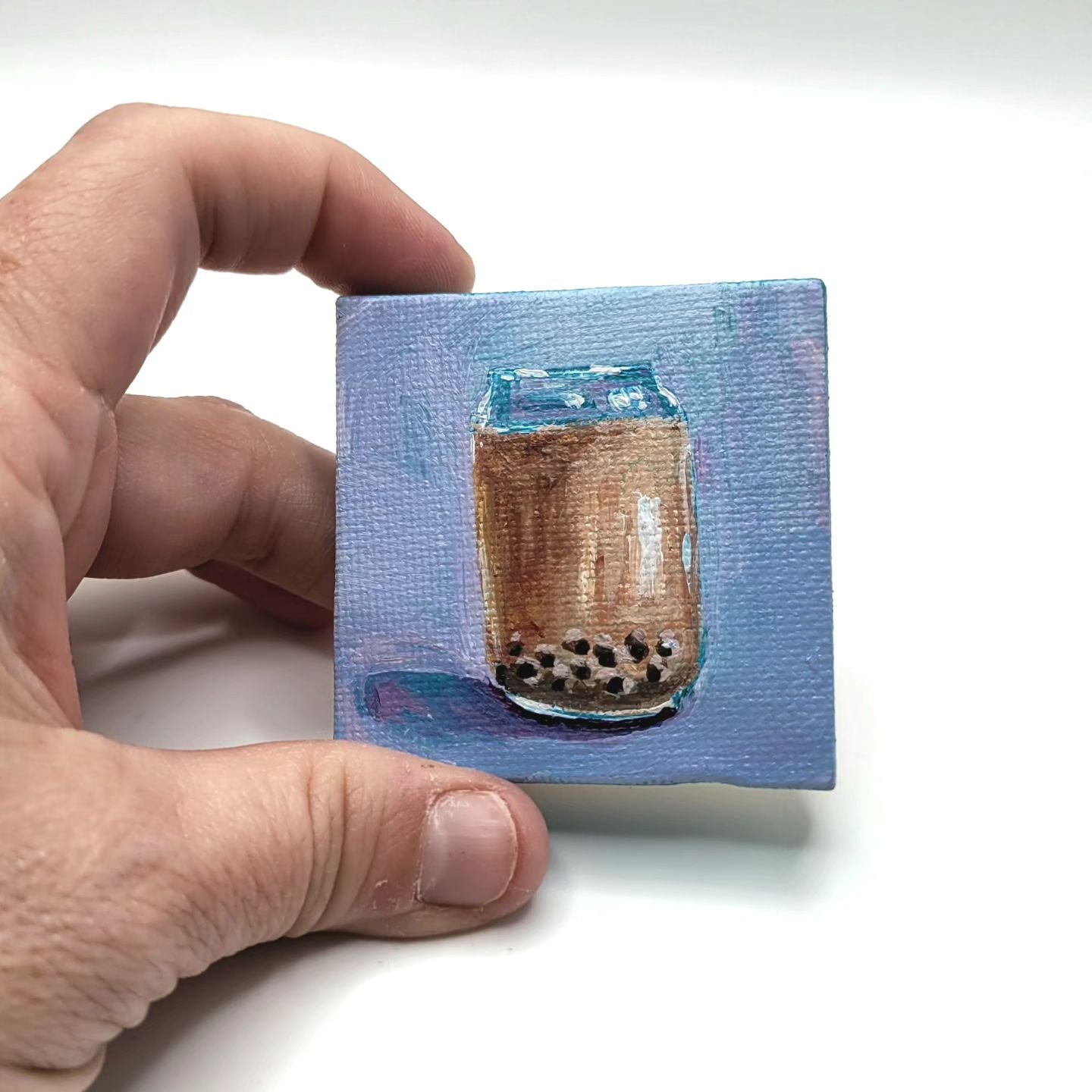 Hand holding 2x2 inch canvas with glass of boba tea on blue gradient background. Kellie Sansone Creates acrylic painting