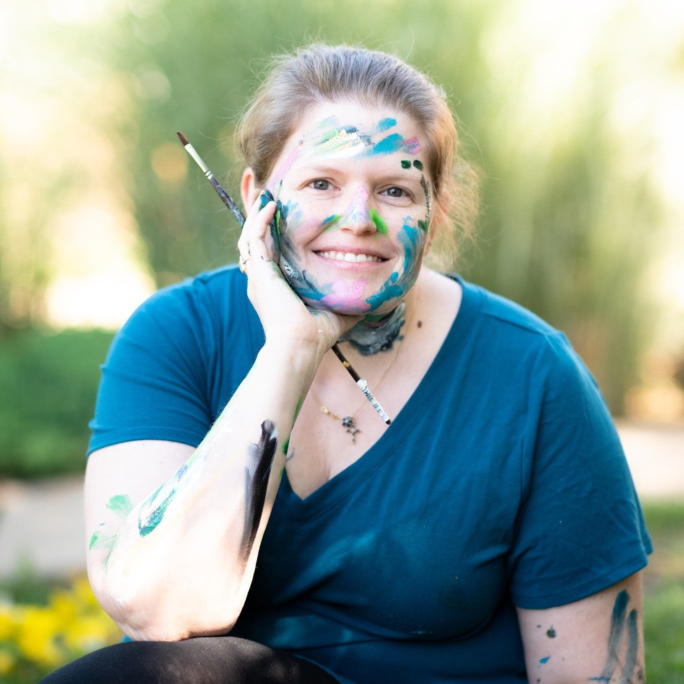 headshot of woman covered in paint holding a paint brush